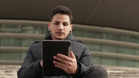 Thoughtful-young-man-using-tablet-while-sitting-outdoor